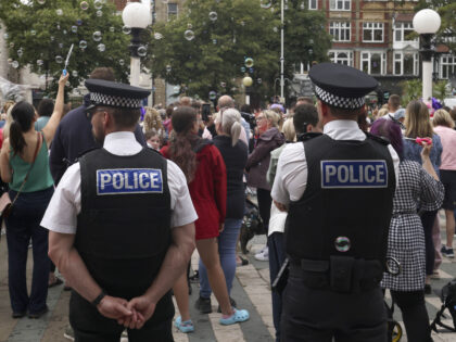 Police officers watch members of the public outside the Town Hall during a vigil to rememb