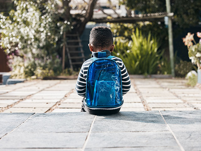 Shot of a little boy sitting outside with his backpack - stock photo