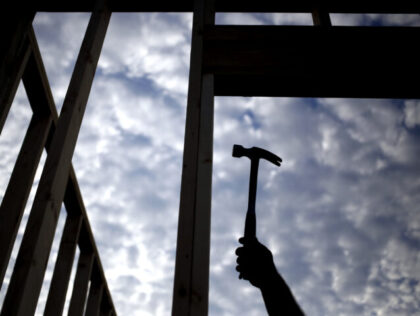 The silhouette of a contractor is seen hammering wood framing for a house under constructi