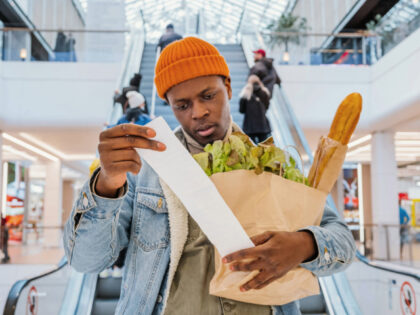 Surprised black man looks at receipt total with food in mall - stock photo