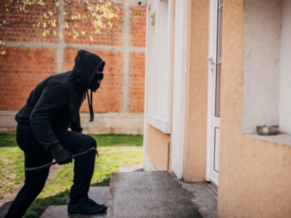 A criminal dressed all in black tries to break into a house with crowbar in hand.